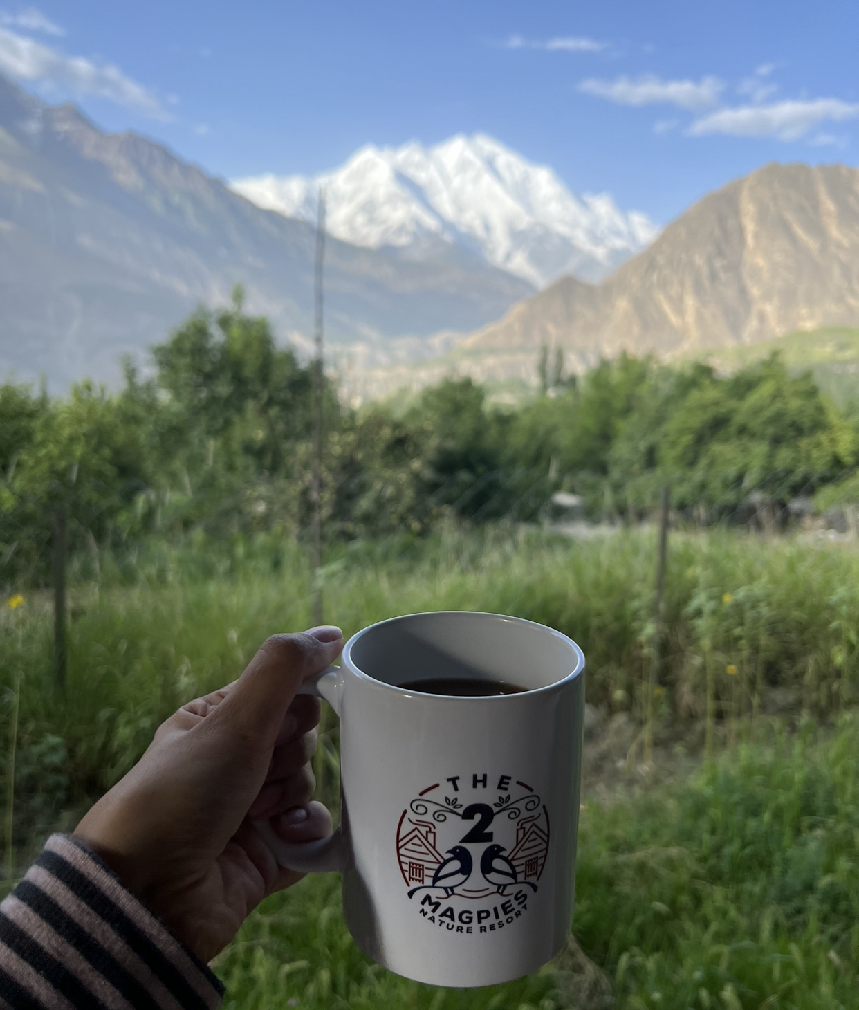 Holding a mug of tea in front of a scenic view of snow-capped mountains in Hunza